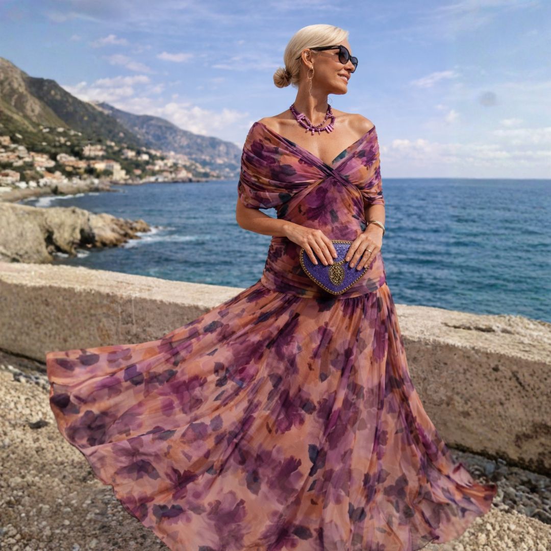 Maya maxi dress in purple floral print, full-length view by the sea
