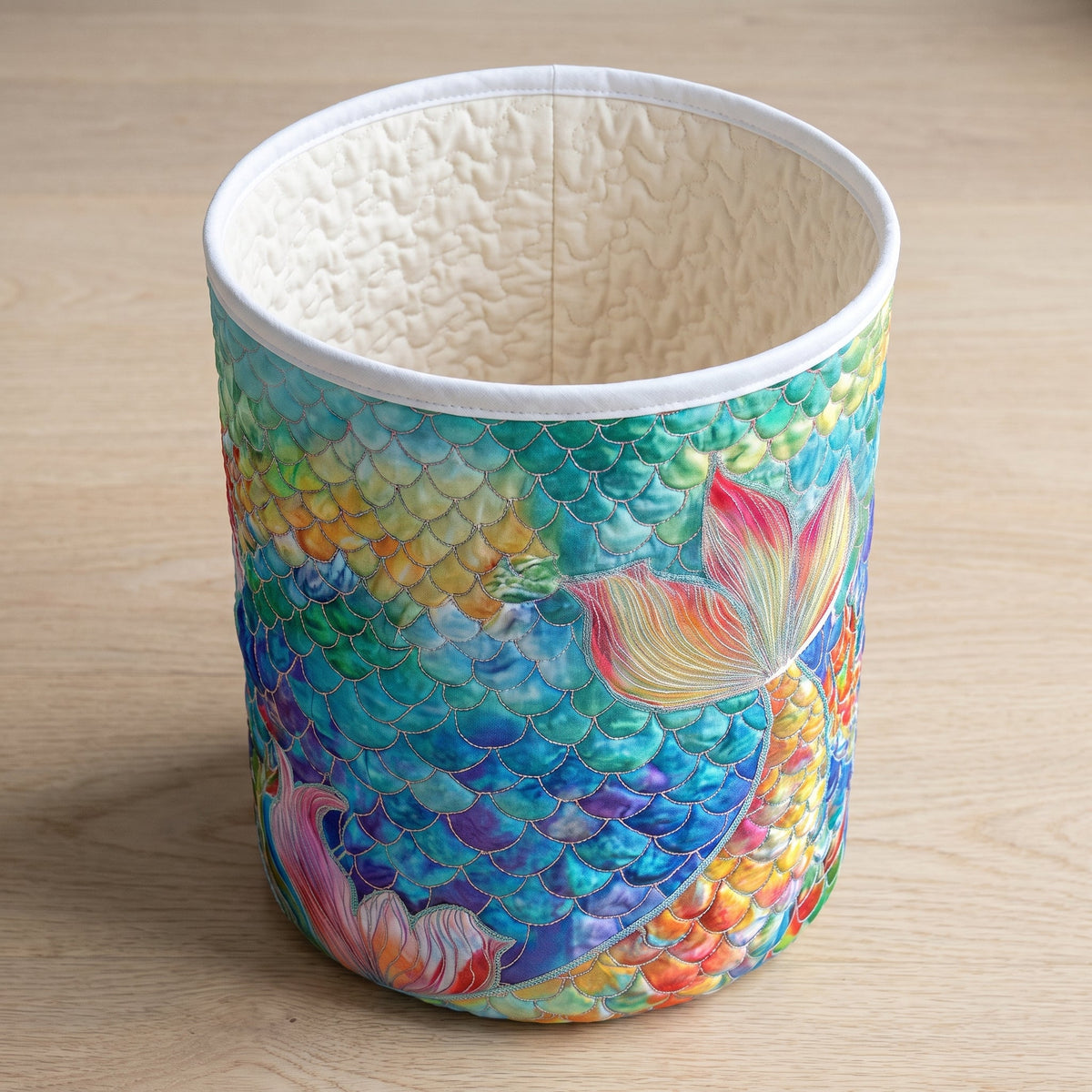 Mattea hand-quilted laundry basket with rainbow mermaid scales and a pink tail, top view showing the quilted lining