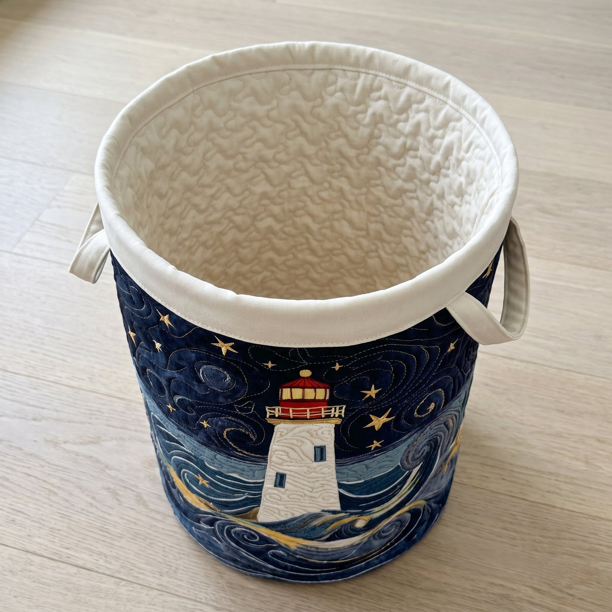 Marta hand-quilted laundry basket with a lighthouse on a swirling night sea, top view showing the quilted lining