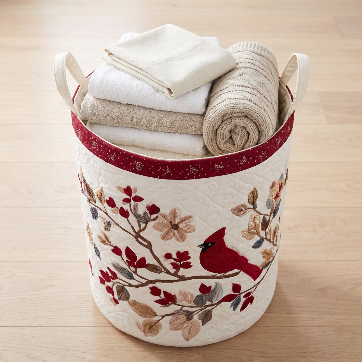 Lucia hand-quilted laundry basket with a red cardinal on a blossoming branch, filled with folded towels