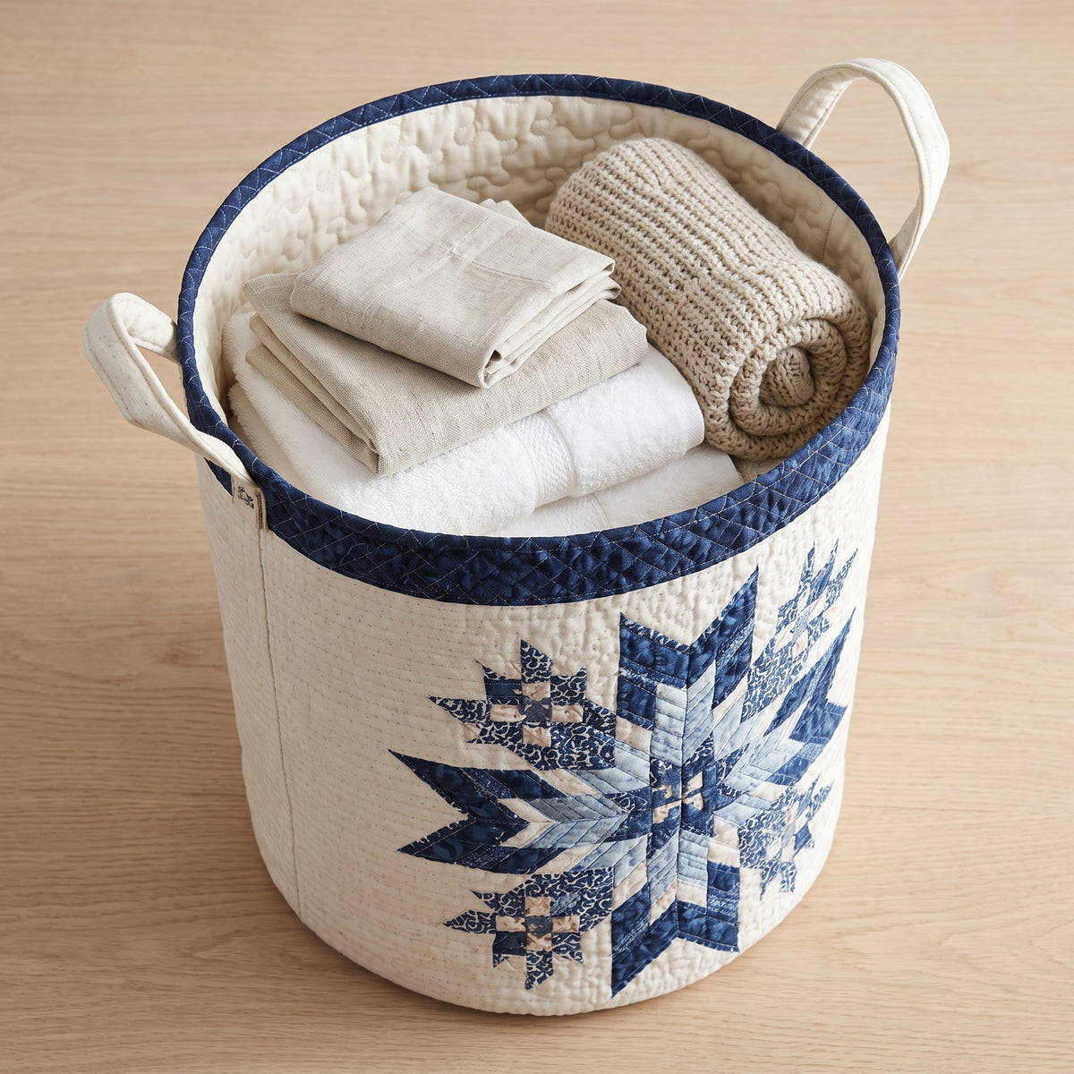 Lorena hand-quilted laundry basket with a navy quilt star snowflake medallion, filled with folded towels