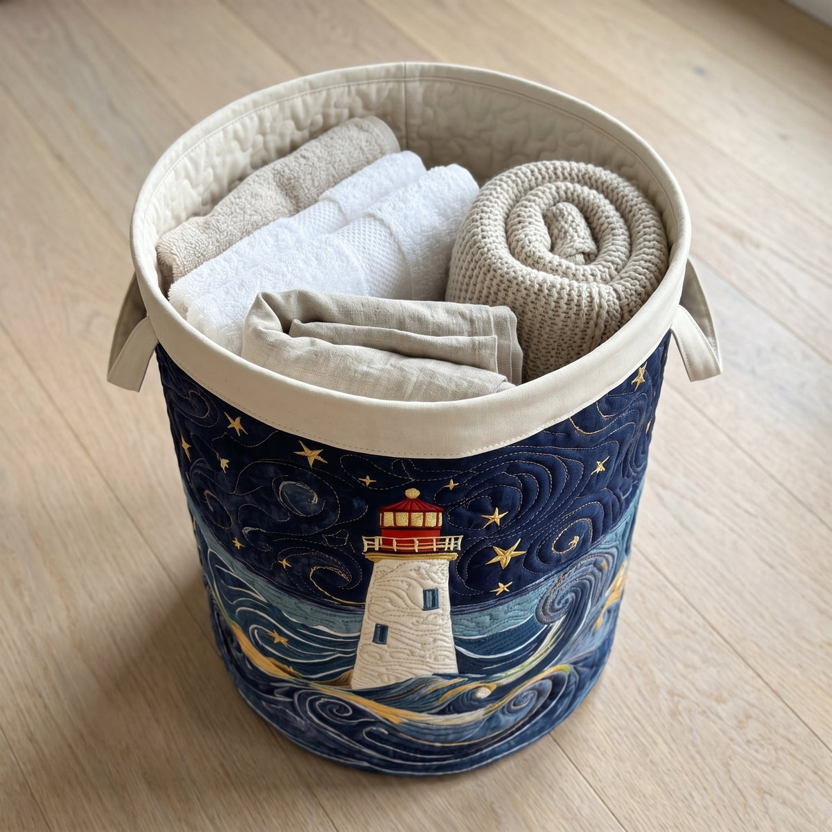 Marta hand-quilted laundry basket with a lighthouse on a swirling night sea, filled with folded towels