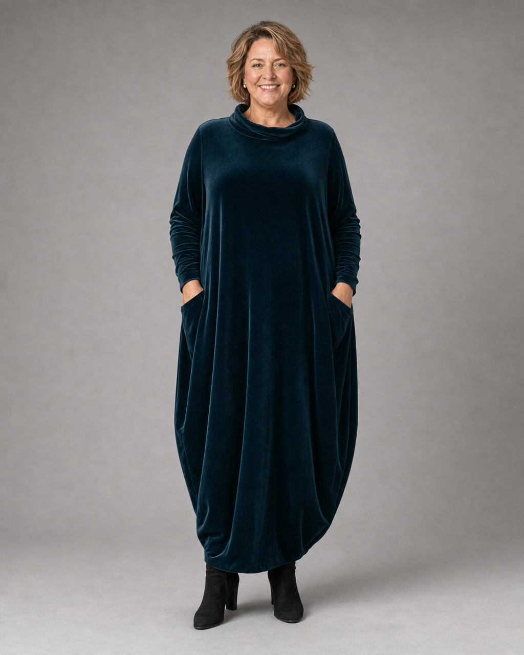 Corisande velvet cocoon maxi dress in navy, worn with hands in pockets