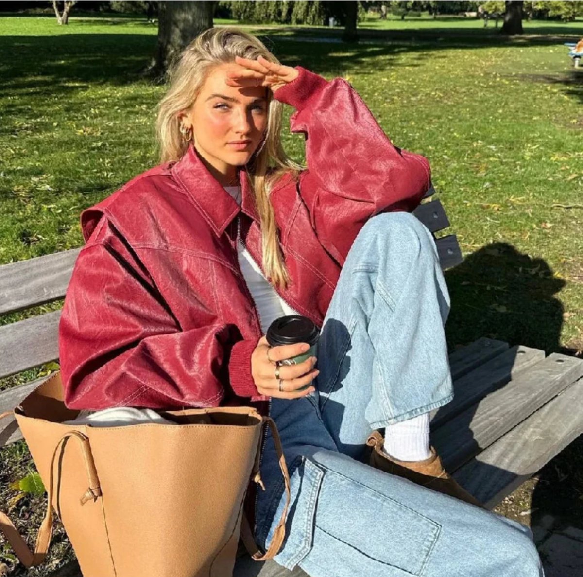 Joyce oversized bomber jacket in wine red, seated on a park bench